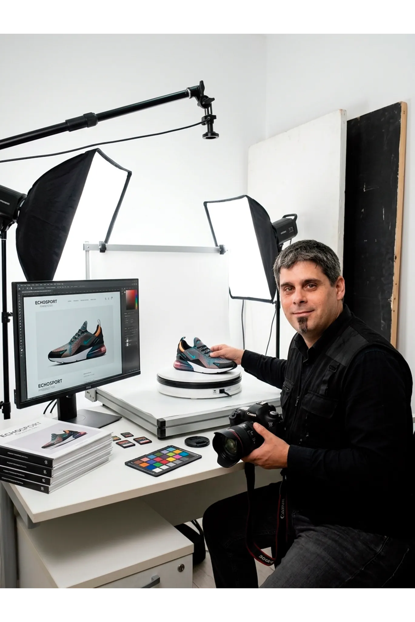 Retrato de Juan Pellicer, consultor de presencia online y creador de contenido visual para E-commerce, sonriendo en su estudio de fotografía de producto con una cámara en las manos y muestras de artículos sobre la mesa de trabajo.